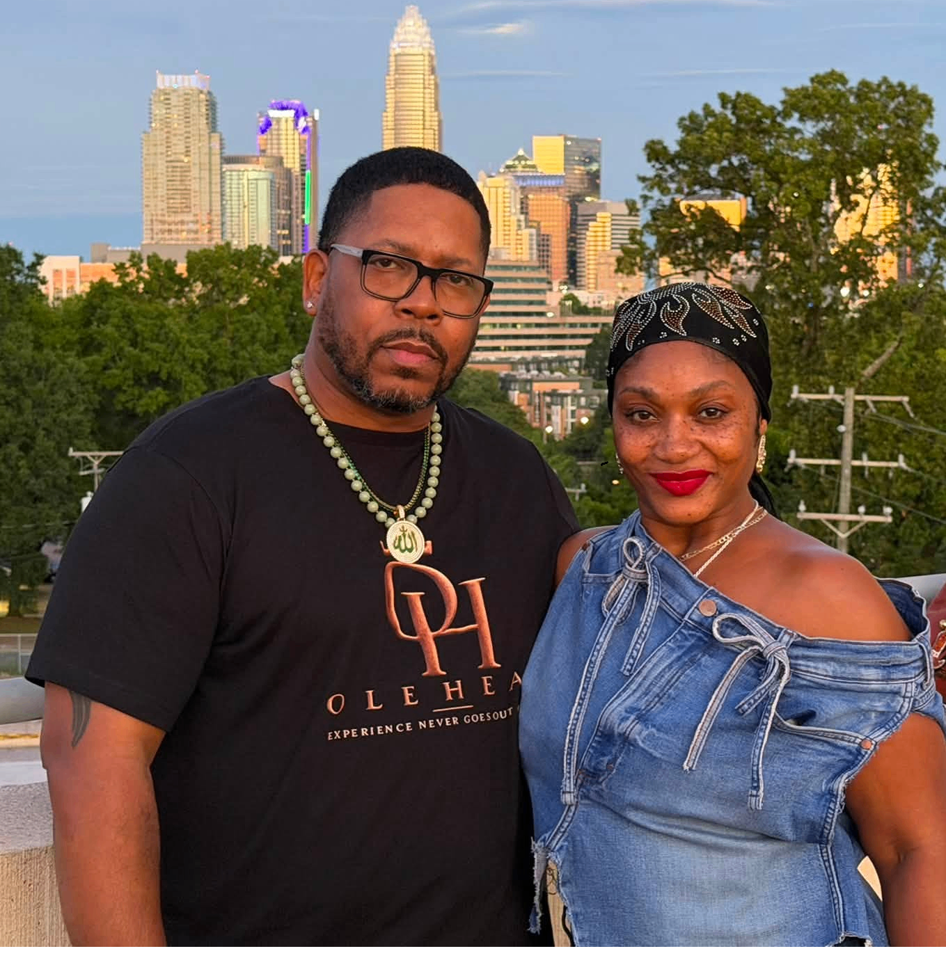 Couple wearing the OLE HEAD signature tee with the Charlotte skyline at golden hour